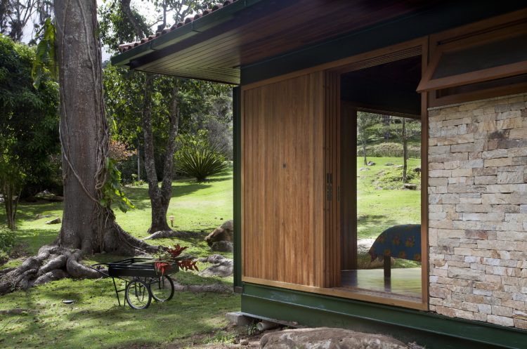 Casa de campo integrada ao lado externo, parede de pedra, esquadria em madeira, vigas pintadas de verde