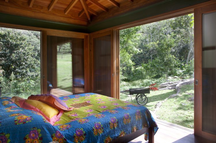 Quarto em uma casa de campo, esquadrias em madeira, grandes vãos que quando abertos, a natureza integra 