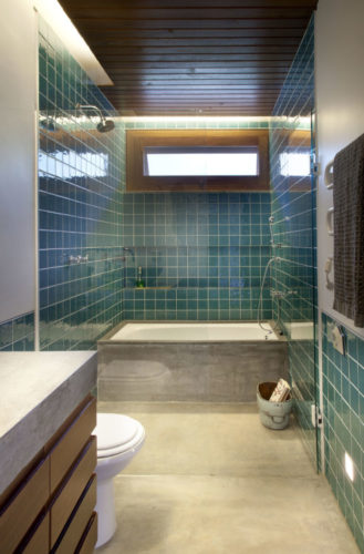 Banheiro em uma casa de campo, meia parede com revestimento azulejo azul , e pra cima, em cimento