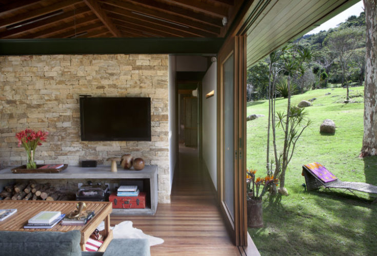 Sala de uma casa de campo, esquadrias em madeira com vãos abertos e espaço integrado a natureza