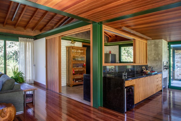 Casa de campo com piso em madeira, cozinha com passa prato e bancada para a sala.