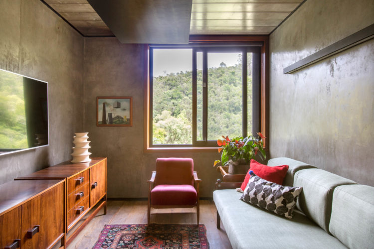 Sala de tv na casa de campo com ares contemporâneos, paredes revestidas com cimento, móveis dos anos 60