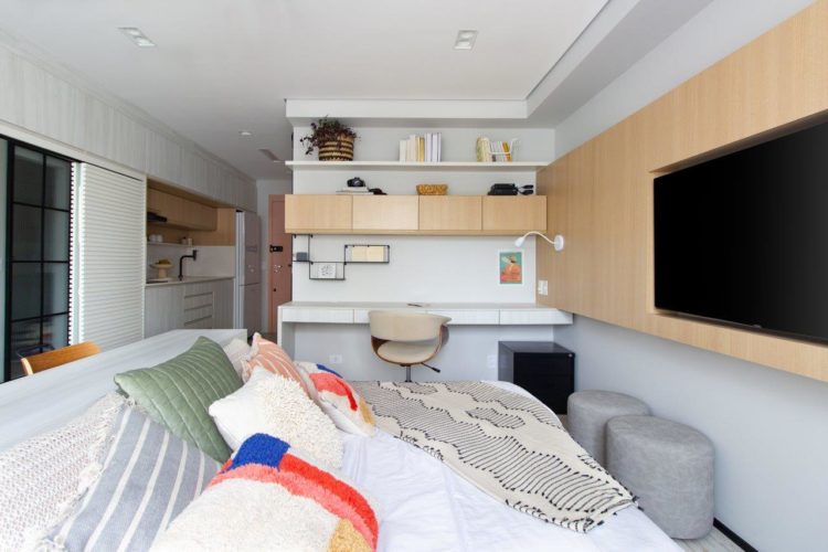 Apartamento de 30m2 em tons claros na decoração, painel de madeira embutida alguns armarios e a tv.