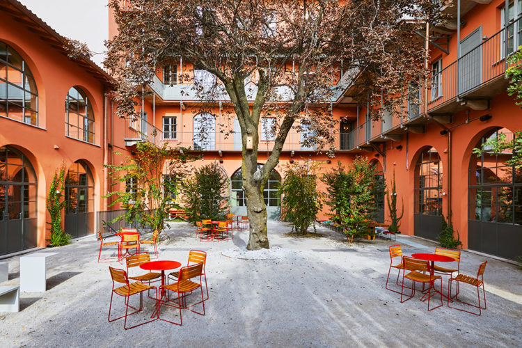 Hostel em Milão. Pátio entre o edifício com planta em L pintado de laranja