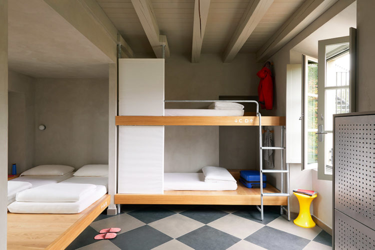 Quarto em um hostel em Milão, beliches em madeira e roupa de cama branca, piso em xadrez preto e branco