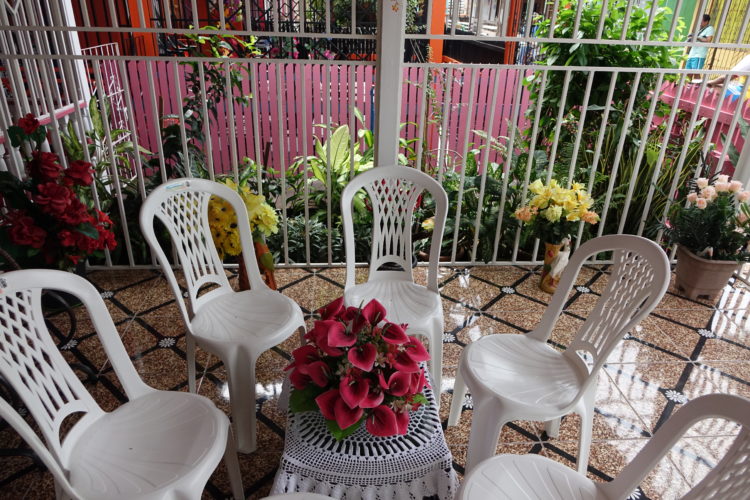 Varanda da casa em Belém do Pará. Cadeiras brancas de plástico em torno da mesinha decorada com flores