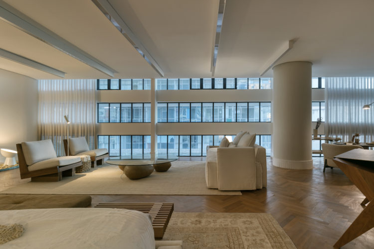 Ambiente da mostra MODERNOS ETERNOS 2022: NO CORAÇÃO DE BH. Em um prédio com projeto de Oscar Niemeyer. Fachada de vidro, pilar redondo no meio do espaço. 