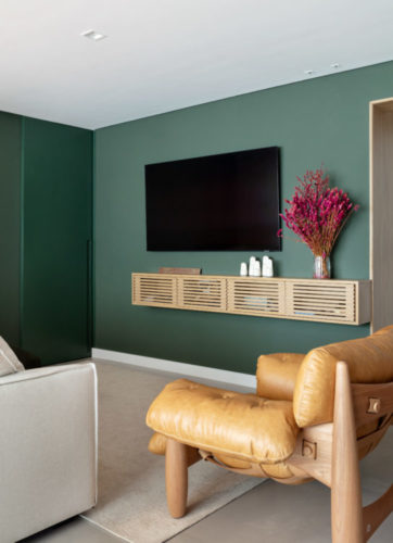 Sala com a parede pintada de verde, e a porta para a área interna do apartamento camuflada na parede pelo pintura 