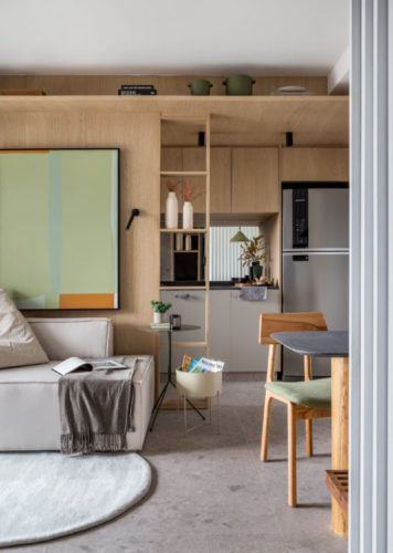 Apartamento de 55m2 na Zona Portuária do Rio. Cozinha integrada a sala, paredes revestidas em madeira, sofá cinza