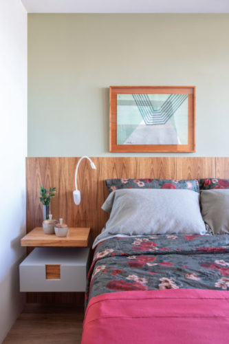 Quarto com parede de fundo na cor verde, e cabeceira da cama em madeira. Enxoval da cama na cor roxa