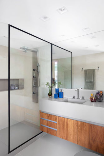 Banheiro com esquadria preta bem fininha, bancada em silestone branco e armários em madeira