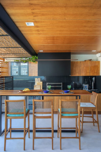 Área gourmet, com teto revestido em madeira, churrasqueira, e mesa alta com banquetas 
