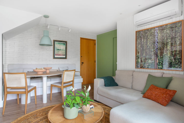 Sala na parte de baixo de uma cobertura duplex, parede de tijolinhos brancos, mesa em formato orgânico, e sofá cinza encostado na parede