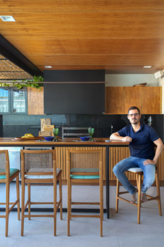 O arquiteto, Henrique Ramalho, sentado no banco, na parte coberta da área gourmet