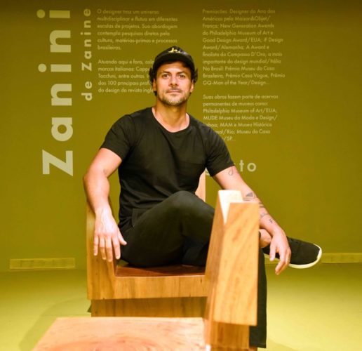 Zanini de Zanine sentado em uma das esculturas de madeira da sua exposição, Iorubá