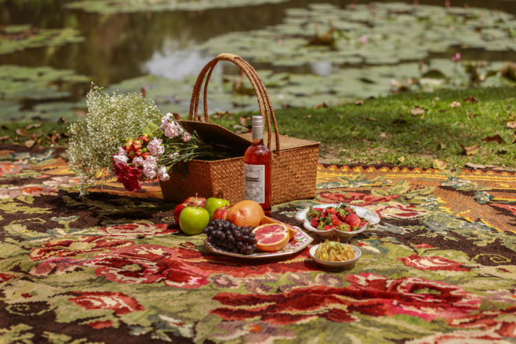 Tapete Kilim Bessarabian, florido, usado como toalha de pic-nic , com um cesto e frutas em cima.