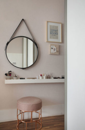 Prateleira na parede, um espelho redondo e um puff, criam ambiente de pendeadeira