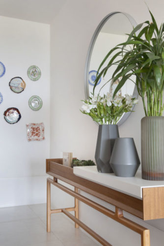 Aparador com vasos de flores e plantas, ao fundo, composição de pratos na parede.