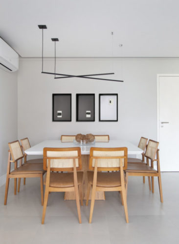 Ambiente de sala de jantar para oito pessoas. Mesa quadrada na cor branca e cadeiras em madeira e encosto de palhinha.