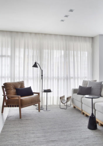 Apartamento decorado em tons claros, poltrona em couro em frente ao sofá cinza. 