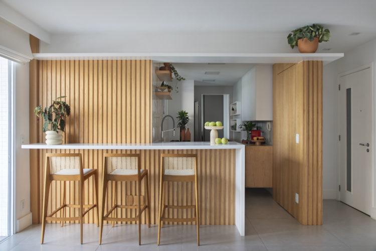 Cozinha integrada a sala, com balcão alto e detalhes em madeira ripada