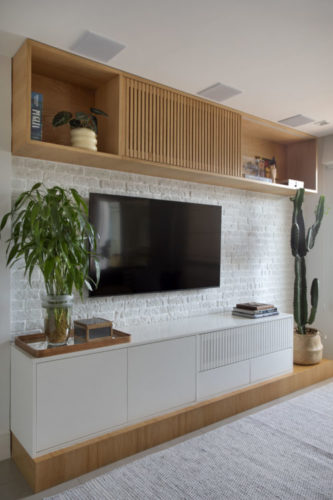 Tv na parede de tijolinho branco, com rack baixo na cor branca, e modelos na parte superior