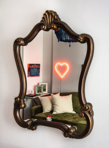 Espelho antigo om moldura em madeira, refletindo nele, um coração em neon
