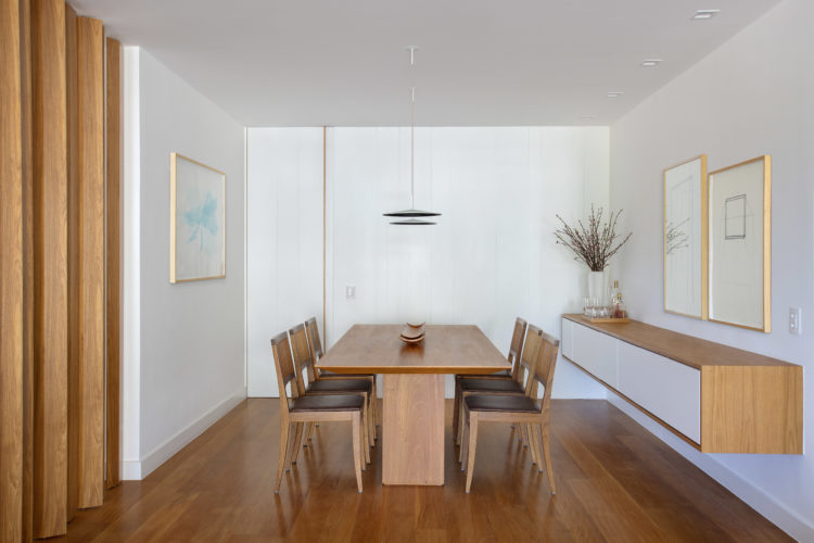 Ambiente de sala de jantar com piso, mesa e cadeiras em madeira. Aparador também em madeira, mas com portas em lacca branca.