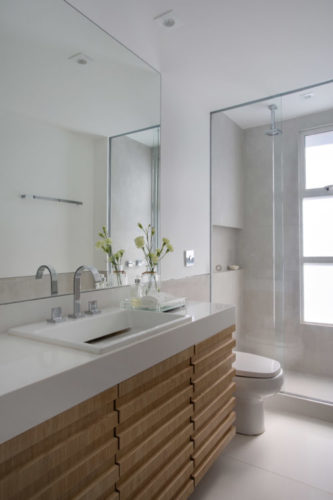 Banheiro com revestimentos na cor branca, e o armário embaixo da bancada em madeira clara
