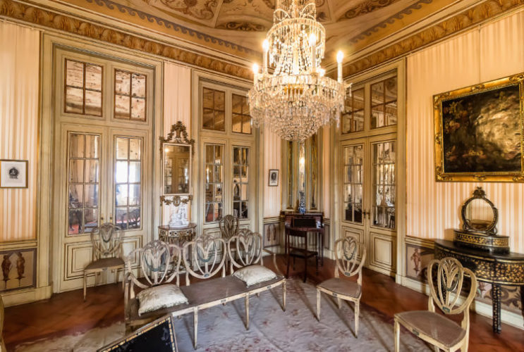 A casa em histórias – A sala de estar. Sala no Palácio Queluz. Decoração com luxo, lustre de cristais no centro do ambiente, paredes forradas em tecido 