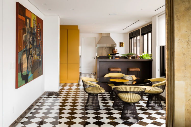 Copa com piso xadrez em preto e branco, balcão alto preto e ao lado, um armário na cor mostarda.