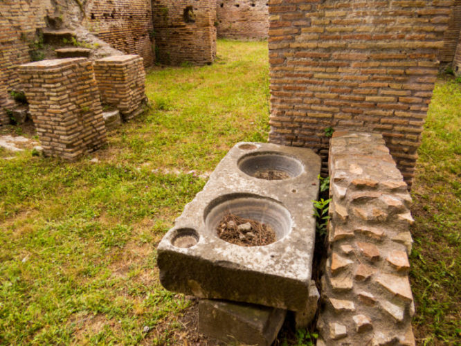 A casa em histórias – A Cozinha. Sitio Arqueológico de Ostia - Itália, com uma pedra contendo dois buracos circulares 