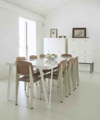Ambiente de sala de jantar, paredes brancas e cadeiras me madeira clara.