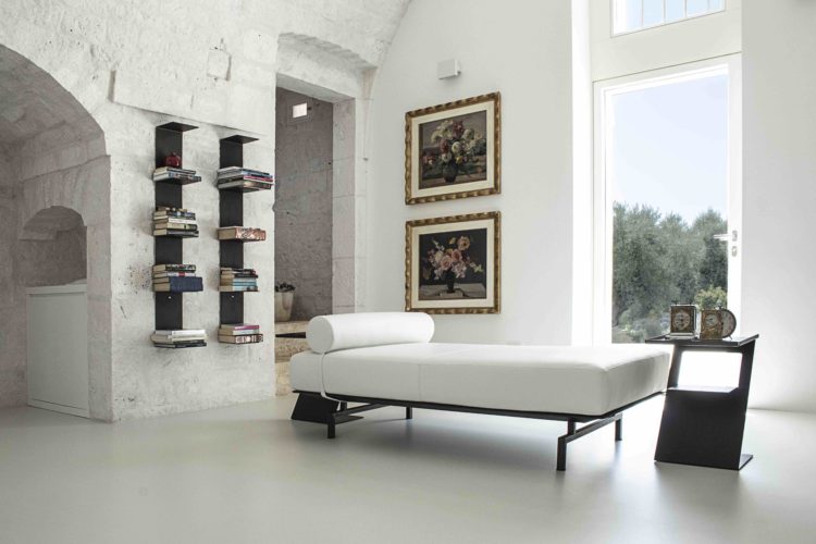 Na Itália, um antigo moinho datado de 1875 transforma-se em uma casa de campo. No interior, paredes em cal, decoração contemporânea, uma chaise em couro branco e na parede, prateleiras com livros. 