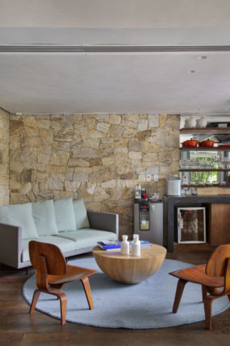 Sala de estar que da apoio ao espaço gourmet na casa de 790m2 no Jardim Botânico. Parede de pedra natural ao fundo.