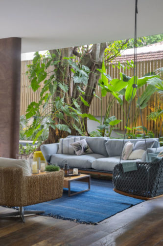 Sala externa integrada com a parte da piscina, na casa no Jardim Botânico. Uma cadeira balanço suspensa na cor azul, e um sofá em azul claro decoram o ambiente 