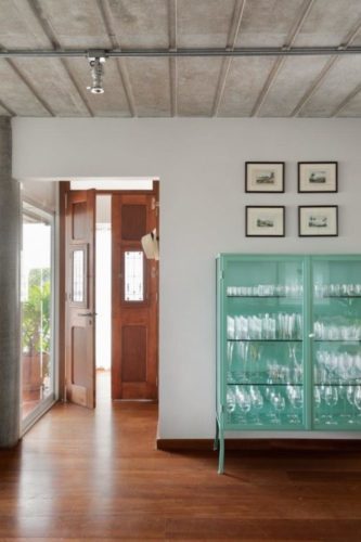 Entrada de um apartamento com porta em madeira, estilo antigo, peça garimpada. Cristaleira em ferro pintado na cor azul turquesa.