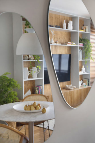 Dois espelhos na parede, em formato orgânico, refletem a decoração da sala 