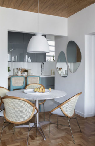 Apartamento de 85m2 com decor claro, cor azul e revestimento em madeira. Mesa de jantar redonda e na parede, dois espelhos no formato orgânico 