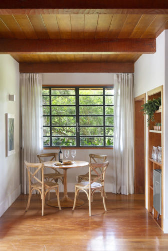 Mesa redonda e cadeiras em madeira, teto revestido com ripas de madeira.