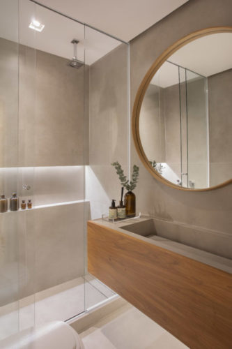 Banheiro revestindo com pintura efeito cimento, espelho redondo e bancada com cuba esculpida revestida em madeira