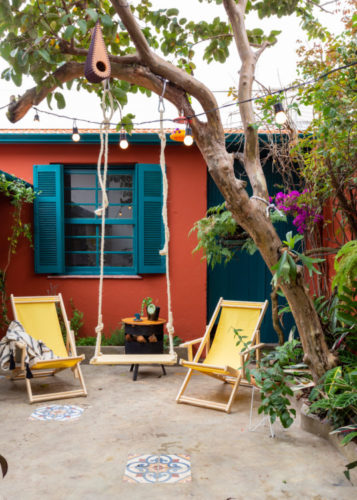 Quintal de casa, parede externa pinta com a cor terracota, janelas com um tom de azul, duas cadeiras de praia decoram o quintal.