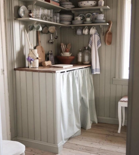 Uma bancada pequena de cozinha estilo campestre, com uma cortina de tecido na parte de baixo, ao invés de armários.