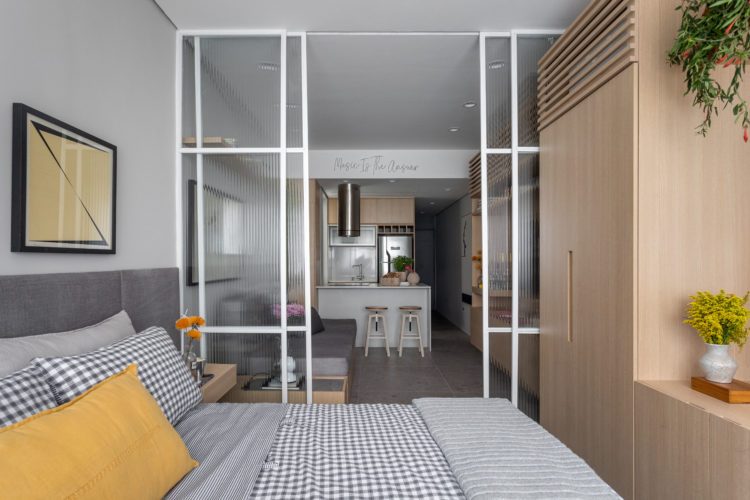 Décor contemporâneo urbano em apartamento com 32m2, divisória, com duas portas de correr em vidro canelado e esquadria branca, separa a sala do quarto