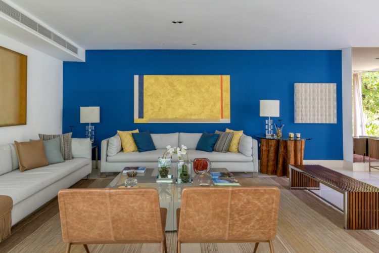 Sala com uma parede pintada de azul, um tela de cor amarela na parede.