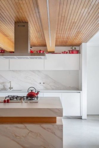 Cozinha estilo minimalista, bancada e armários brancos, com teto em madeira ripada 