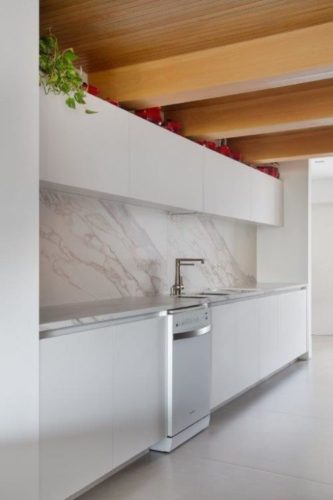 Cozinha ampla e décor minimalista em apartamento na Vila Mariana. Cozinha toda branca, armários e bancada, apenas teto revestido em madeira