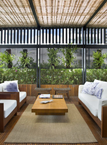 Paisagismo para o terraço em uma cobertura no Leblon, com pergolado, piso em deck de madeira e sofás brancos