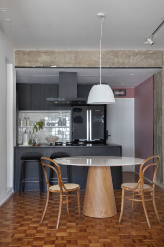 O primeiro apartamento de um jovem médico. Cozinha integrada a sala, com armários e bancada na cor preto, na parede da cuba, um nicho grande revestido com azulejos brancos. Na frente, mesa redonda e duas cadeiras Thonet.