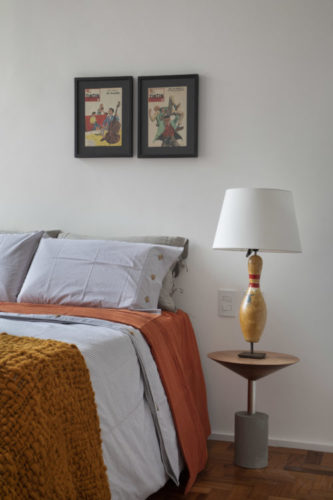 Ao lado da cama, uma mesa de cabeceira com um abajur em cima que tem como base, um pino antigo de boliche.